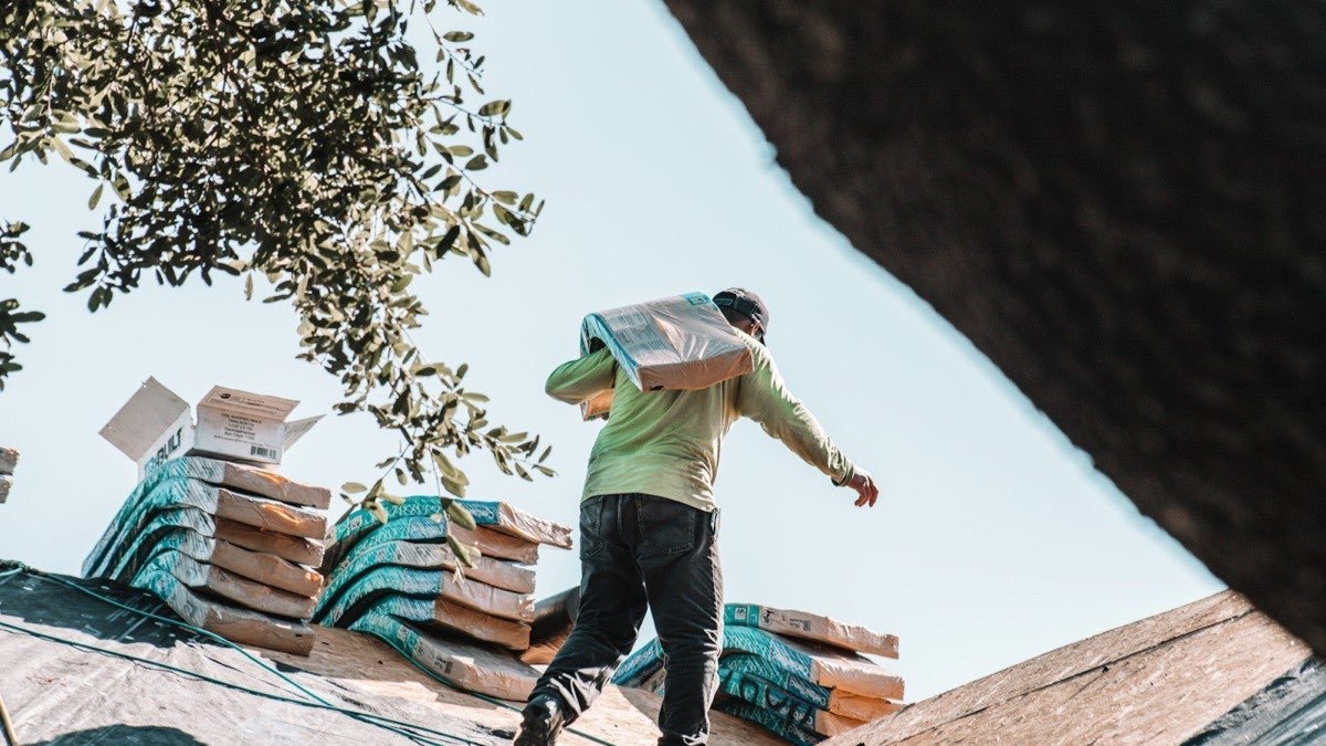 Roofing worker carrying a bundle of shingles across a residential roof