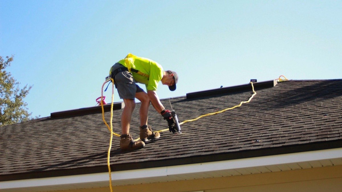 Roofer fastening shingles on a residential roof on a clear day