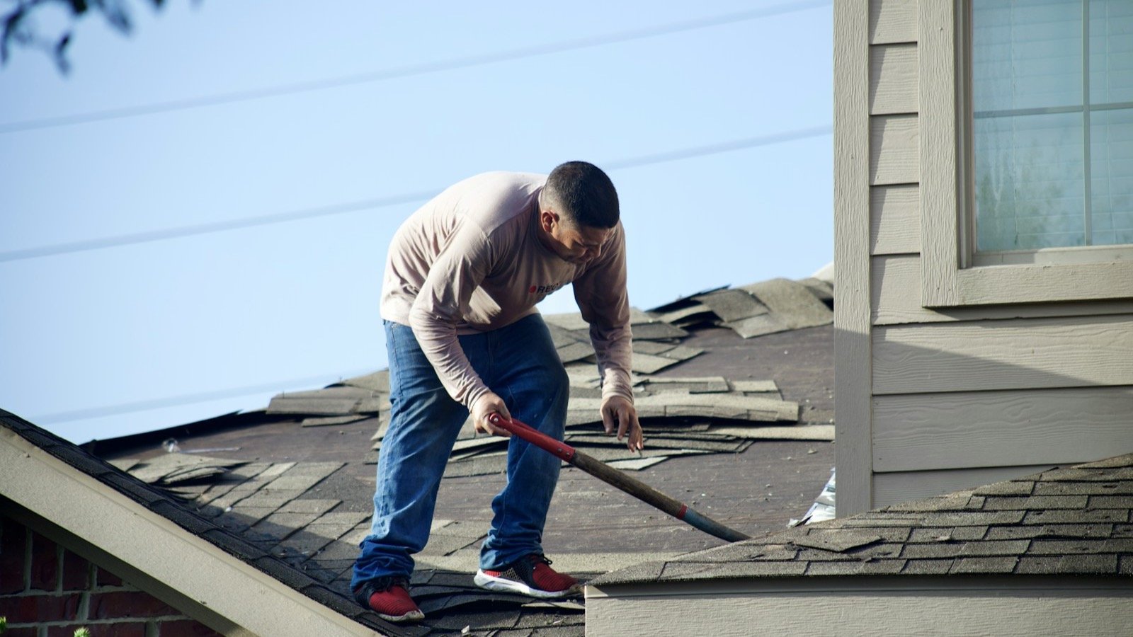 Worn asphalt shingles being stripped from a residential roof