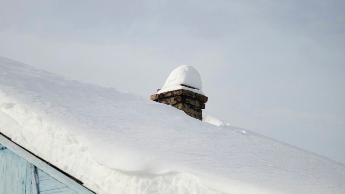 Snow sitting on a sloped residential roof and chimney in winter