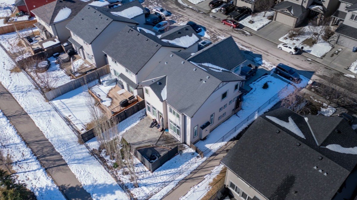 Aerial drone view of two-storey homes with grey asphalt shingle roofs in a snowy Alberta subdivision